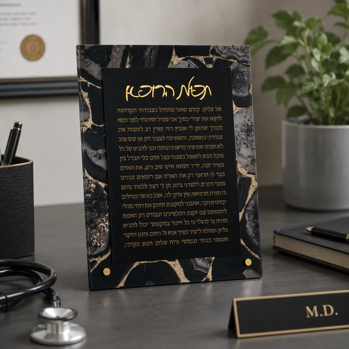 Black agate tabletop plaque with gold veining featuring Hebrew Birchas Harofeh prayer text, displayed on office desk with stethoscope and medical nameplate.