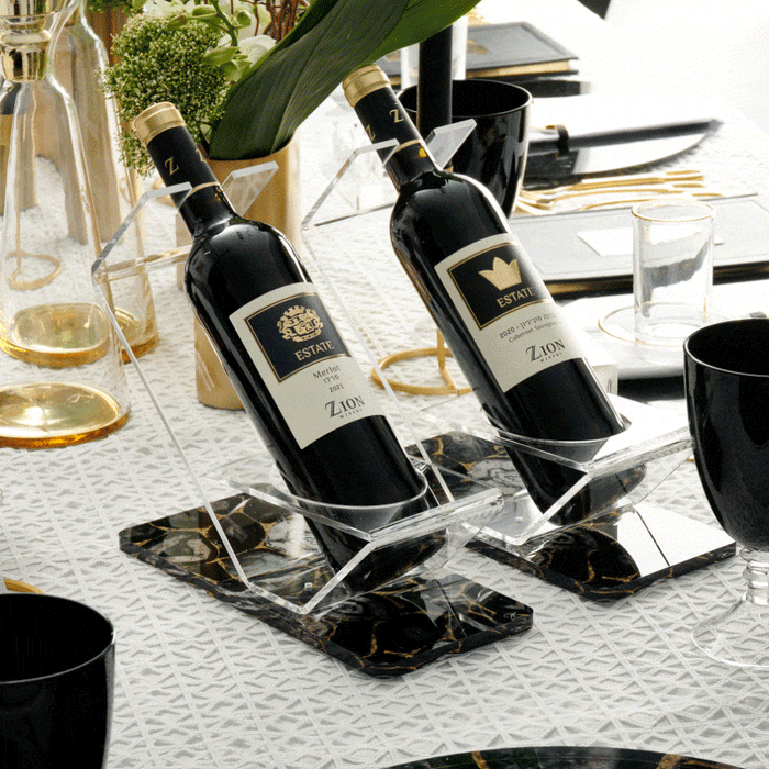 Black agate wine stand holding two bottles of Estate wine on a formal white table setting with glassware and greenery.