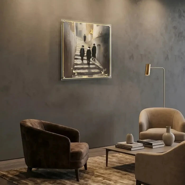 Alleyways painting by Batya displayed above a black armchair in a modern living room with neutral gray walls and natural lighting, showing Jerusalem architecture in a framed artwork.