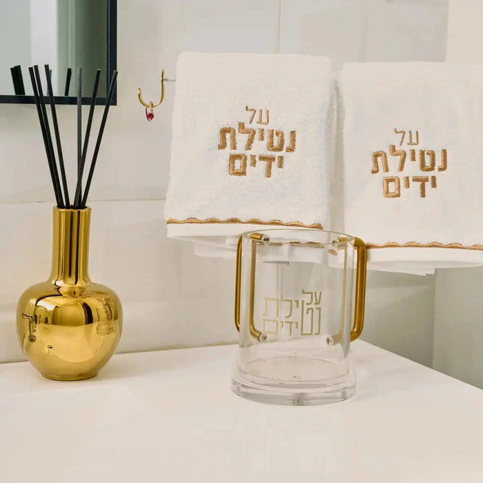 Clear glass Aura Vase Diffuser with gold accents and Hebrew text, displayed with matching gold vessel and black diffuser reeds on white surface.