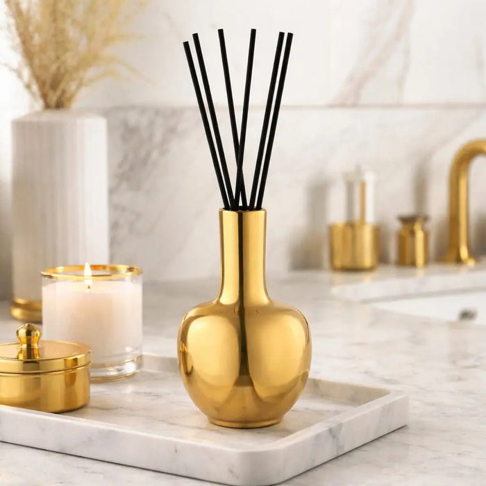 Gold Aura Vase Diffuser with black reed sticks on marble surface, surrounded by candles and home decor accents.