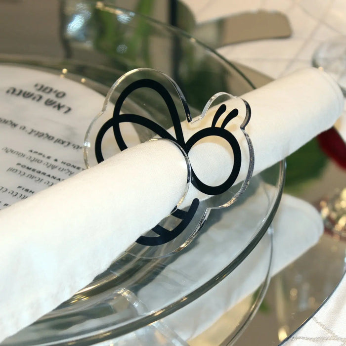 Black bee-shaped napkin rings holding rolled white napkin on formal place setting with glassware and tableware visible.