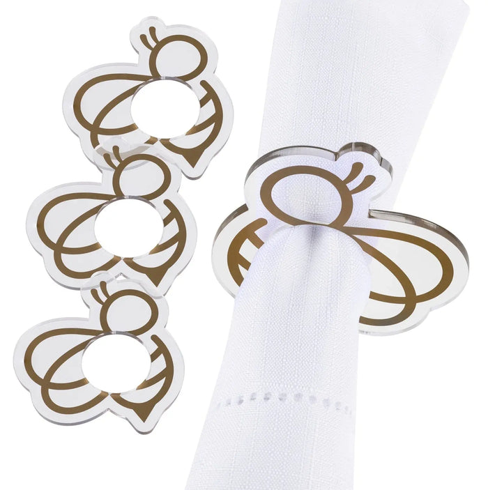 Set of three gold bee-shaped napkin rings holding white napkins, featuring decorative curved metal details on a white surface.