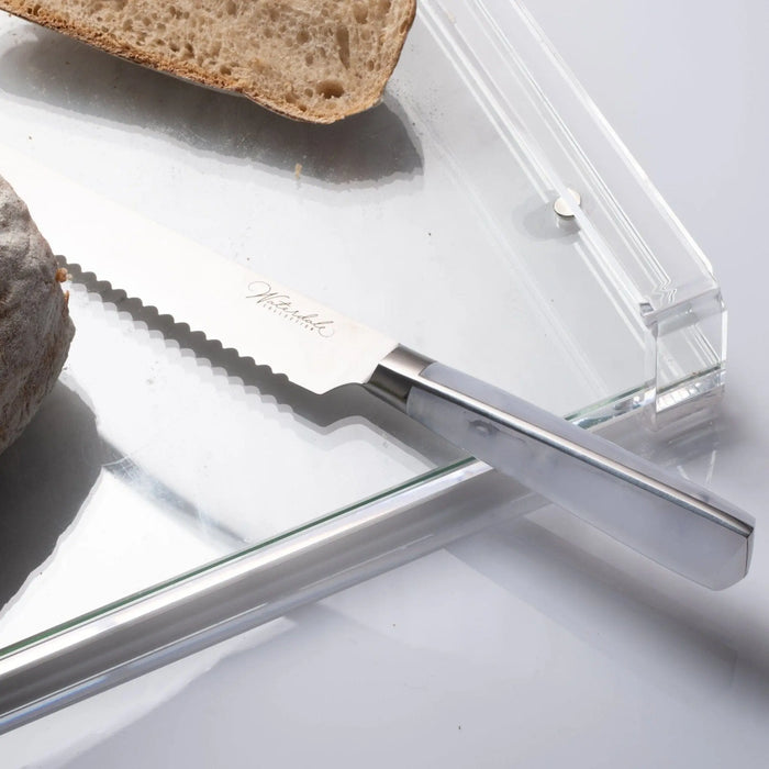 Waterdale Collection serrated bread knife with stainless steel blade on white surface next to sliced bread and cork trivet.