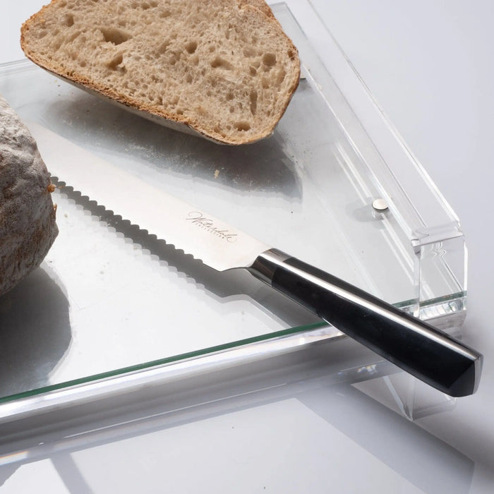 Waterdale Collection bread knife with serrated blade and black handle, shown with sliced whole grain bread on white surface.