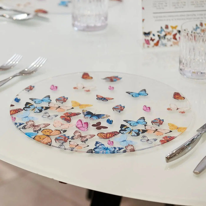 Colorful butterfly chargers arranged on white table, featuring vibrant illustrated butterflies in blue, pink, yellow and orange tones by Waterdale Collection.
