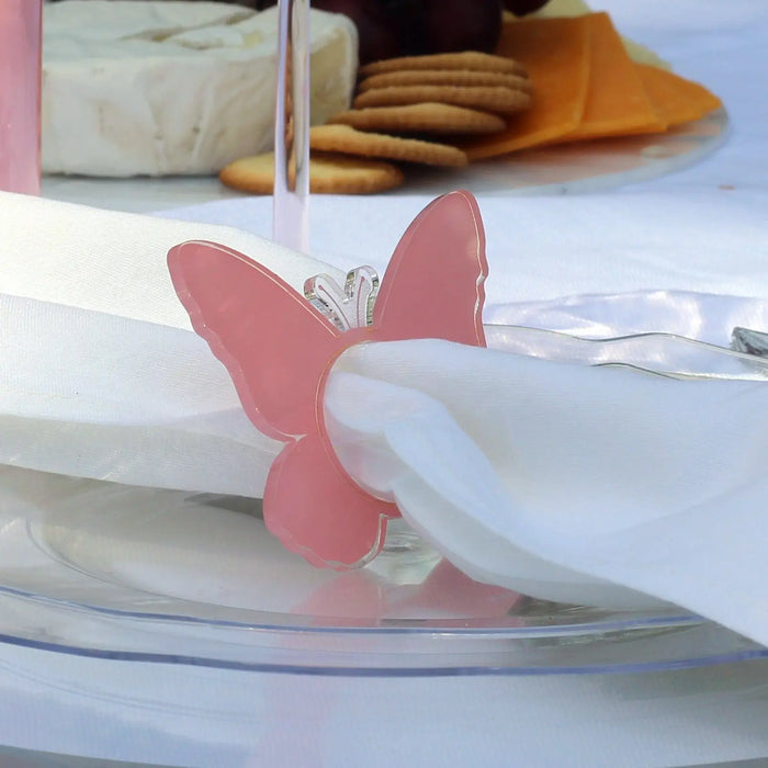 Pink butterfly napkin rings holding white napkins on a place setting, with tabletop décor visible in background