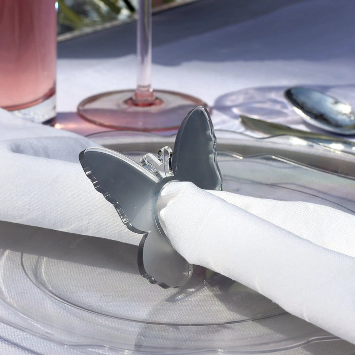 Silver butterfly napkin rings holding white napkins on a table setting with pink goblets and place cards nearby.