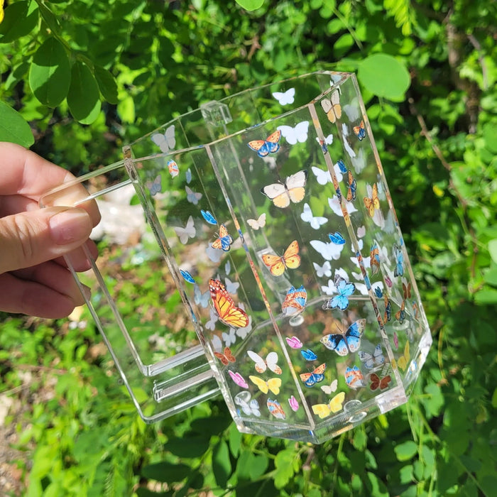 Crystal washing cup with colorful butterfly design and scattered gemstone accents, displayed on green foliage background