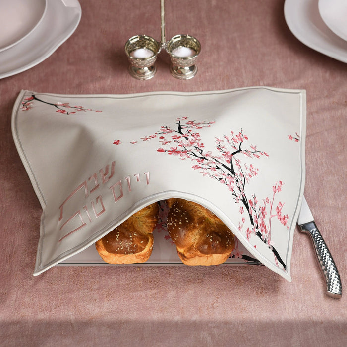 Cherry Blossom Challah Cover in cream with delicate pink floral design, displayed on dining table with bread and place settings.