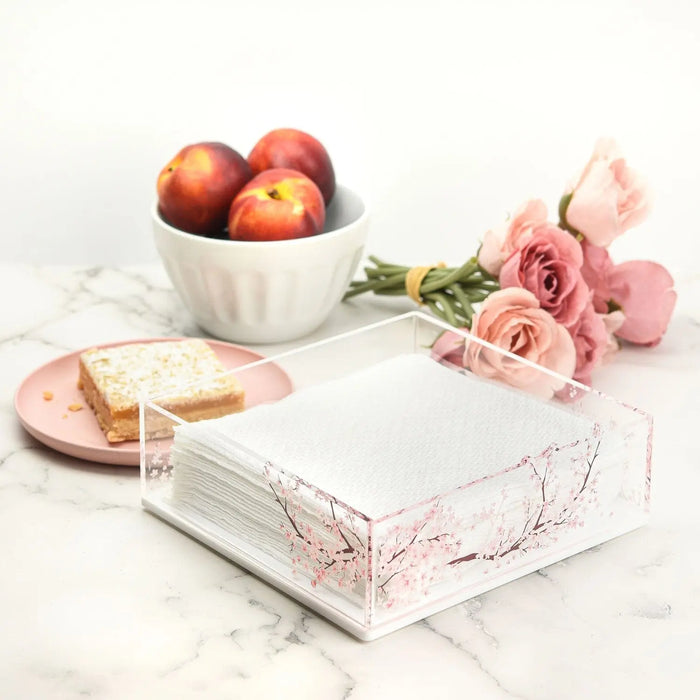 Cherry Blossom Napkin Holder in white marble with pink floral design, displayed with apples, roses, and bread on marble surface