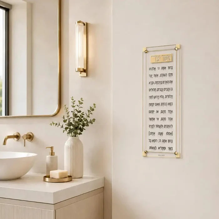 Classic 2.0 Asher Yatzar wall art in cream displayed above bathroom sink with gold fixtures and white flowers.