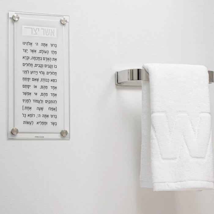 Classic 2.0 Basics Asher Yatzar wall art in black and gold text on white acrylic plaque, displayed above bathroom towel rack.