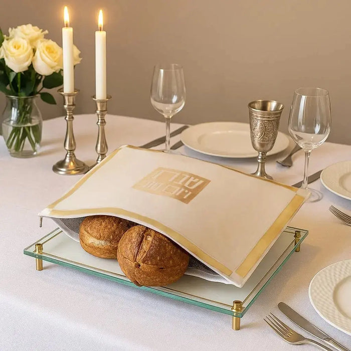 Classic 2.0 Challah Pouch Cover in white and gold leather displayed on a dining table with bread, wine glasses, and table settings for Shabbat.