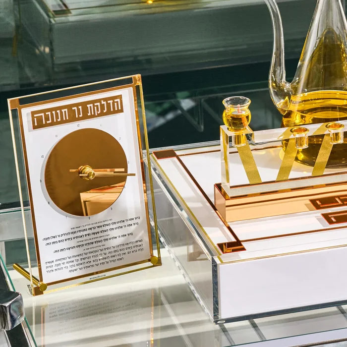 Gold Chanukah Brachos Clock styled on a glass shelf with a menorah tray and an oil jug, set for Hanukkah candle lighting
