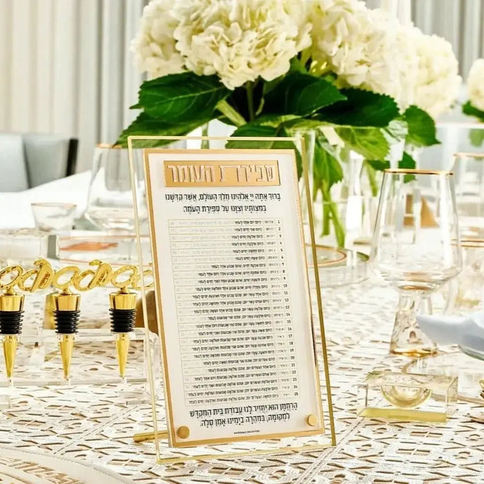 Classic 2.0 gold Sefiras Haomer tabletop plaque displayed on white flowers and table setting for Pesach holiday