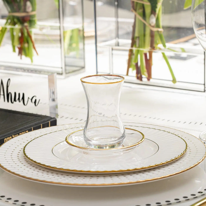 Classic glass cup and saucer with gold rim detail, set on white plate with table setting and fresh greenery