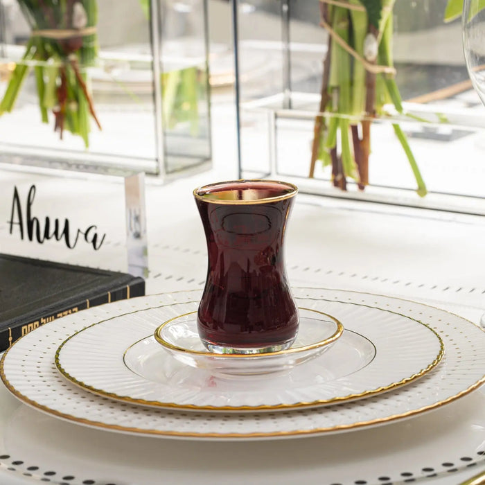 Classic glass cup and saucer filled with dark wine, featuring gold rim detailing on white plate, elegant Pesach tableware set