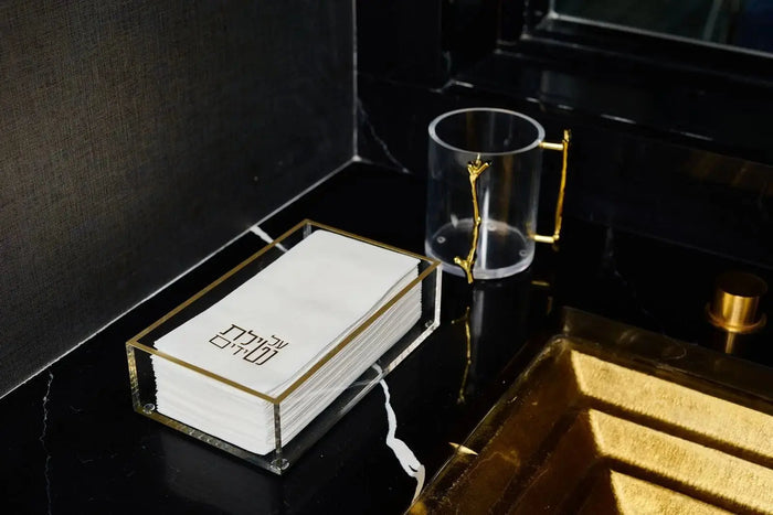 Classic Guest Towel Holder in brushed gold metal with white ceramic base, displayed on black vanity shelf with bathroom accessories.