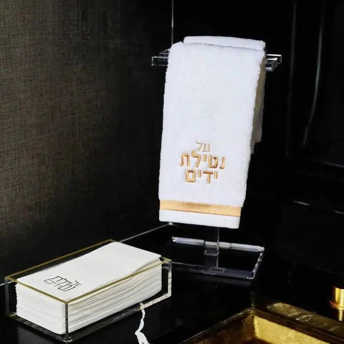 Waterdale Collection classic hand towel in black with gold embroidered design, displayed on acrylic stand with matching towel storage box below