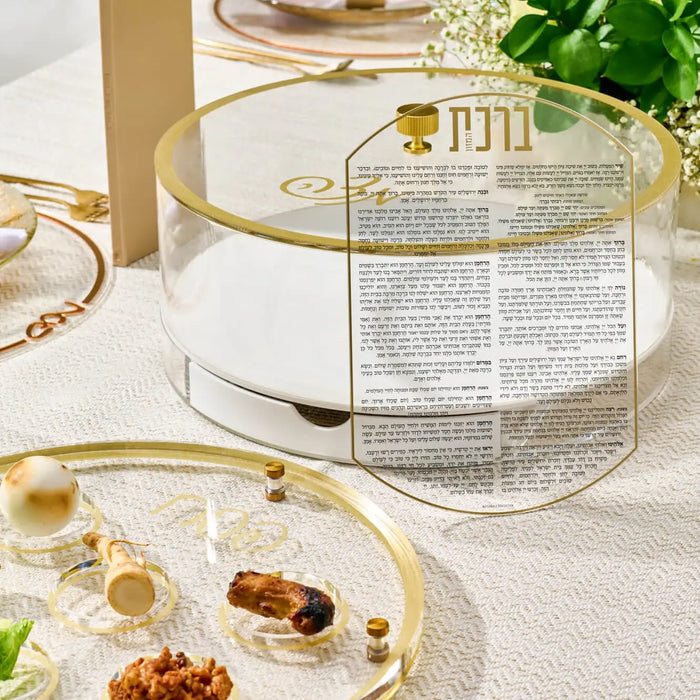 Classic Script Bencher Set Matzah Box in clear lucite with gold accents, displayed with ceremonial plate and greenery for Passover.