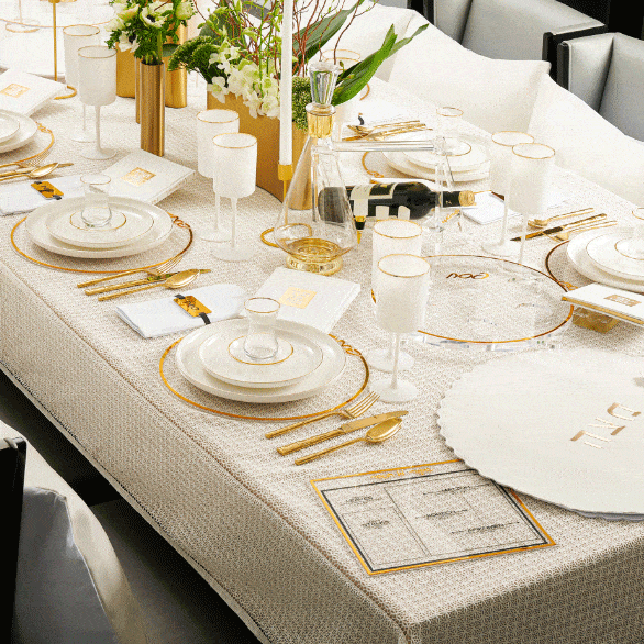 Gold and silver Classic Shiurim Cards displayed on elegant place settings at a Pesach table with white linens and gold accents.