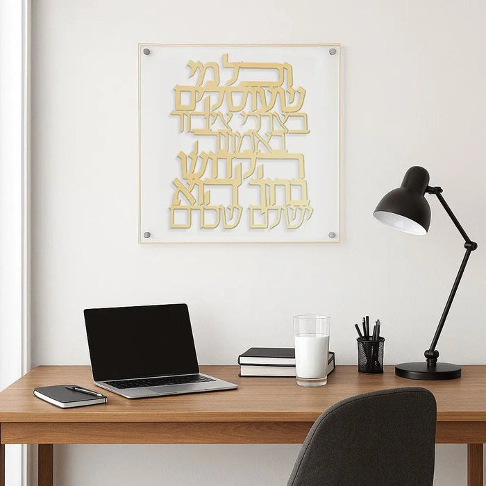 Gold foil floating wall art with Hebrew text by Waterdale Collection, displayed above wooden desk with laptop and black lamp.