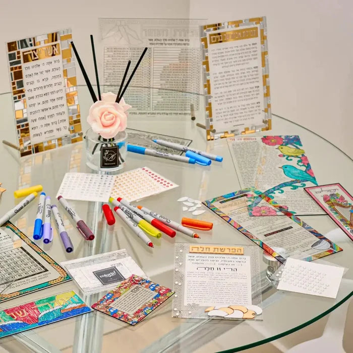 Clear lucite Kiddush card with colorful decorative border, displayed among markers and Hebrew prayer sheets on a white surface.