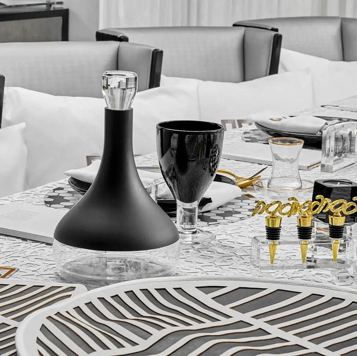 Black contemporary wine decanter on white bedding with wine glasses and gold accents, elegant tabletop styling