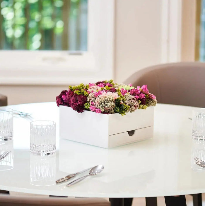 White ceramic vase bencher set with pink and purple flowers displayed on modern office desk by window