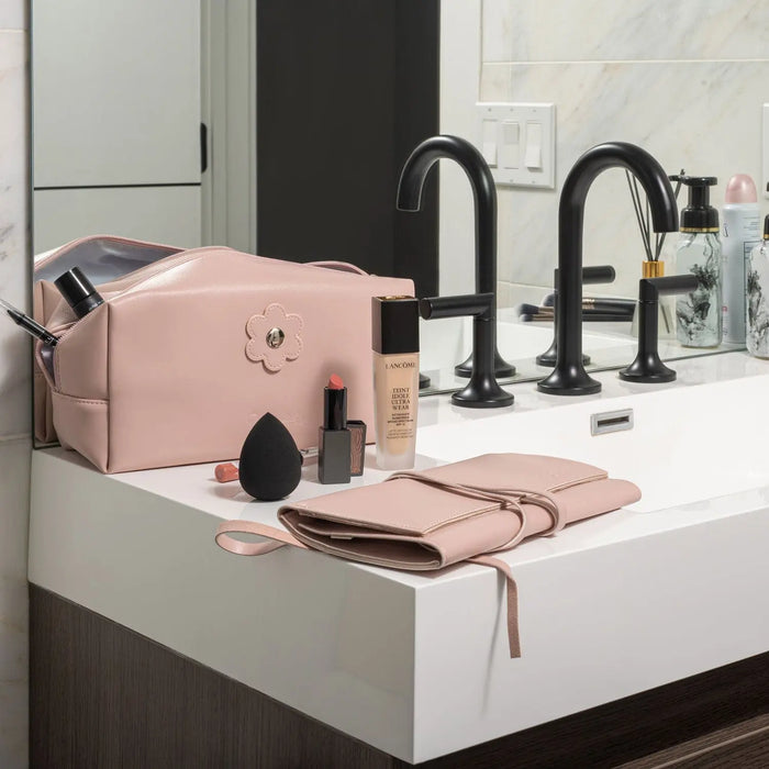 Pink leather cosmetic bag from Waterdale Collection displayed on bathroom vanity with black faucet and accessories nearby.