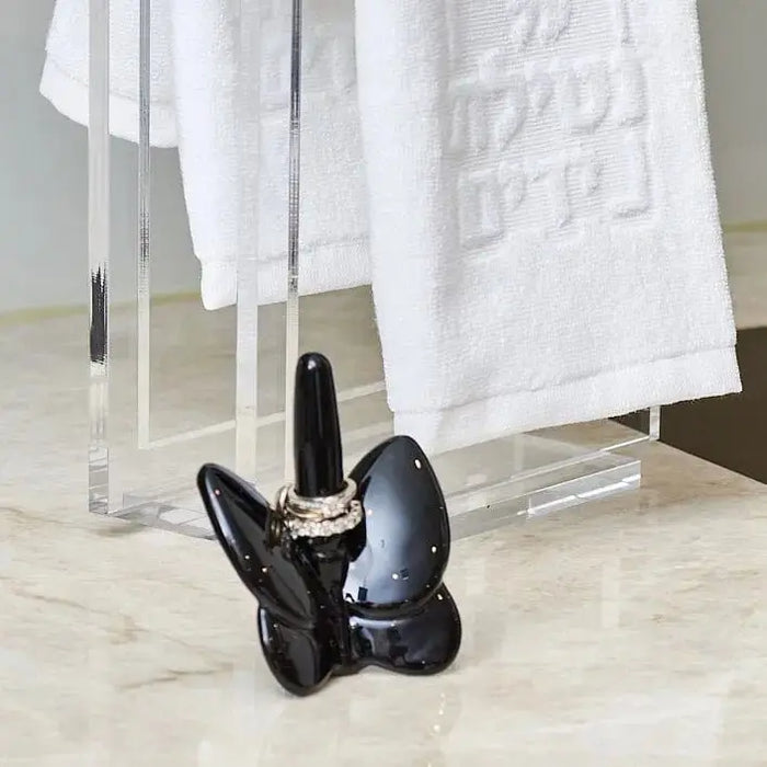Crystal butterfly ring holder in black displayed on a marble surface with white towels in the background