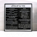 Black and white custom bris card with Hebrew text displayed in clear lucite frame, showing elegant typography and design layout for Jewish ceremony invitations.