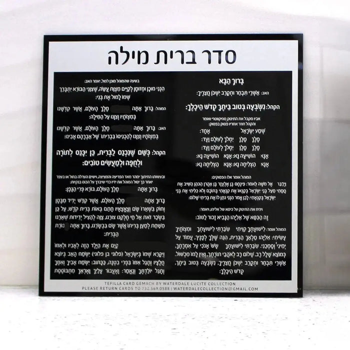 Black and white custom bris card with Hebrew text displayed in clear lucite frame, showing elegant typography and design layout for Jewish ceremony invitations.