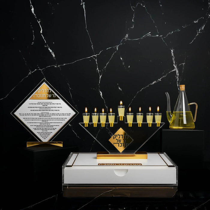 A Waterdale Collection Chanukah set-up on black - the glass oil jug, a gold menorah and the diamond match holder on its white and gold Lucite base