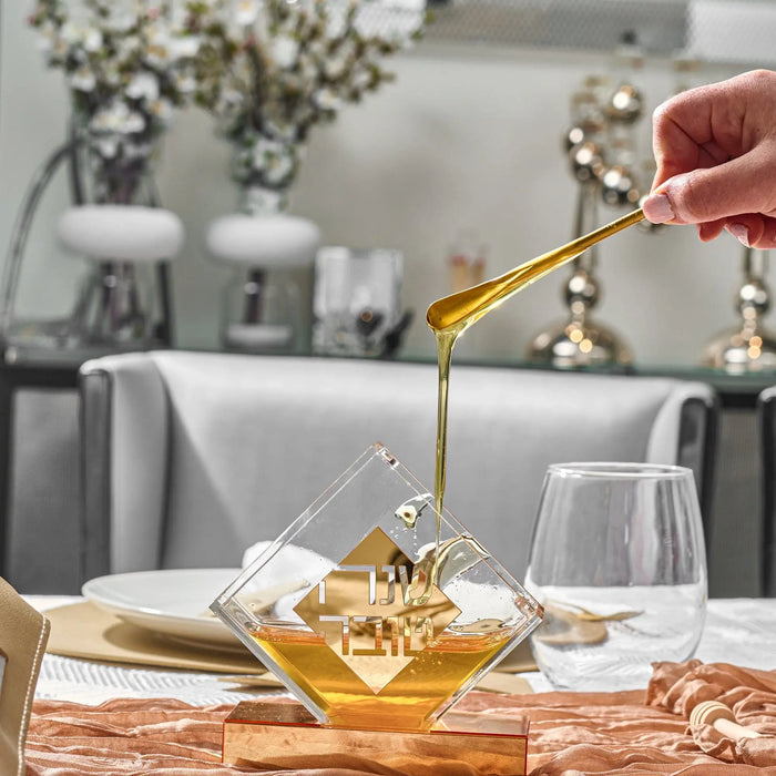 Diamond-shaped honey dish in gold tone with honey dipper, displayed on table with place setting and flowers.