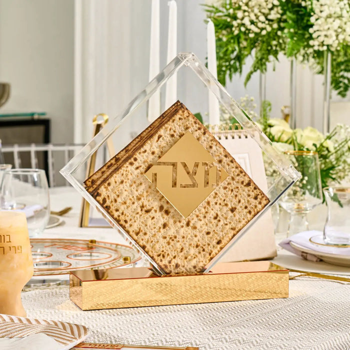 Diamond Matzah Box in woven tan and white with metal accents, displayed on a white table with Passover place setting and fresh greenery.