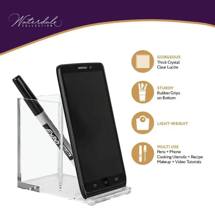 Black and clear acrylic double pen and phone holder by Waterdale Collection, displaying smartphone upright with two pens stored in side slots on tabletop.