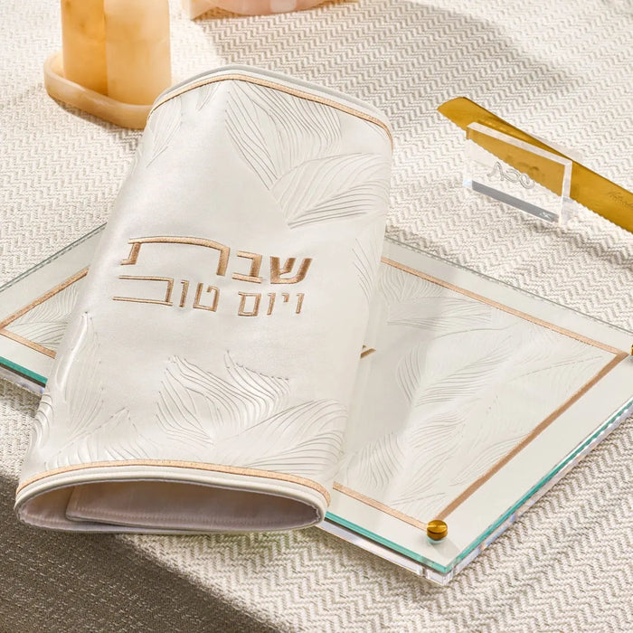 Embossed leaf challah board in cream leather with gold accents, displayed with shabbat items on a neutral surface