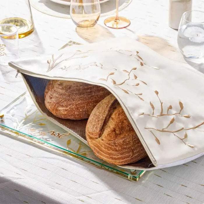 Embroidered leaf challah board and matching pouch set displayed with fresh bread on a white linen tablecloth with table settings.