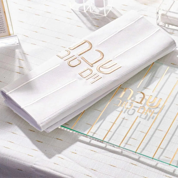White embroidered lines challah cover with gold accents on leather, displayed flat on shabbat table setting.