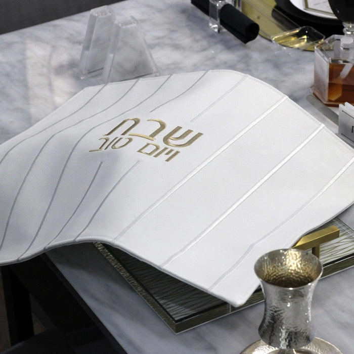White embroidered lines challah cover with gold accents, displayed on a table setting for Shabbat meals.