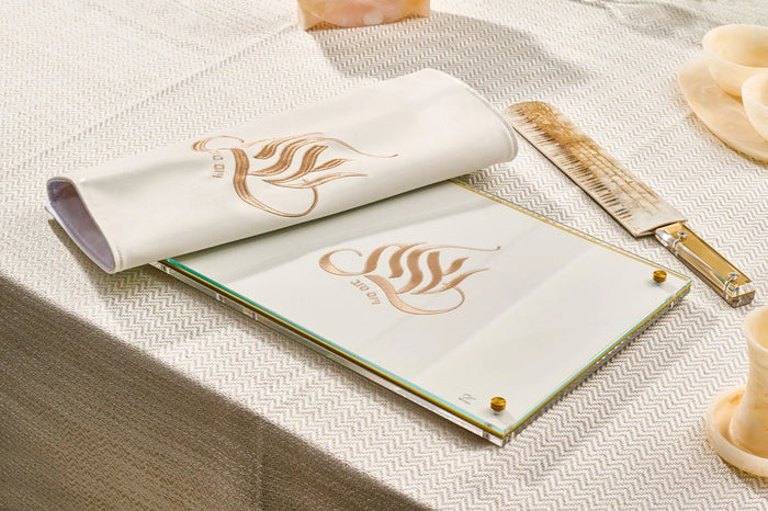 Embroidered Regal Challah Board with gold leaf design on cream leather, displayed with challah cover and wooden serving pieces on table.
