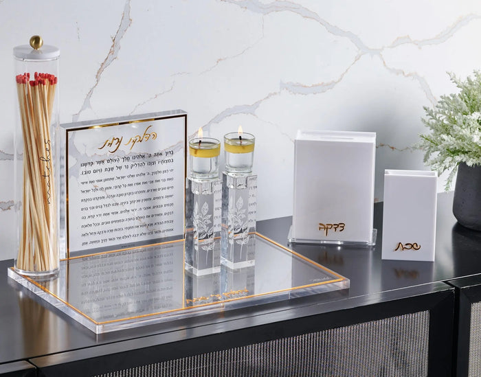 Pair of clear crystal candlesticks with engraved design displayed on black surface alongside candles and Shabbat items
