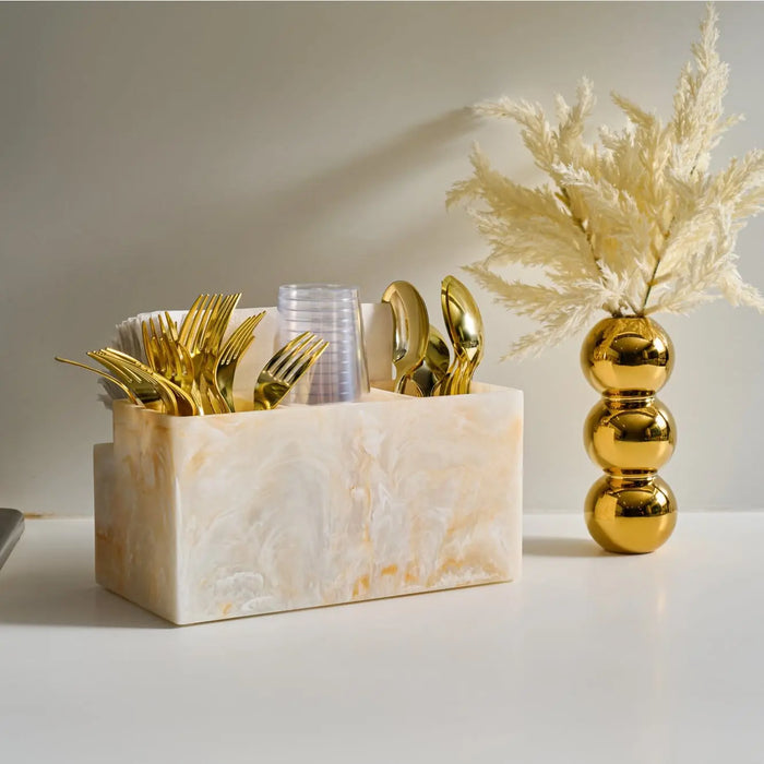 Faux pampas grass in gold vase next to marble cube with gold decorative accents on white surface