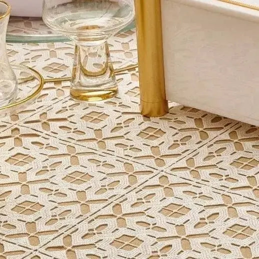 Filet crochet lace tablecloth in cream with geometric cutout pattern, displayed on a floor with gold accents visible.