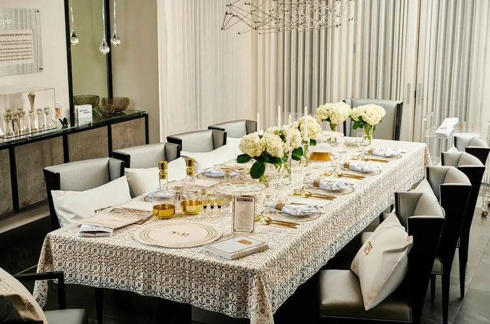 Filet crochet lace tablecloth in cream displayed on a formal dining table set with place settings and white flowers.