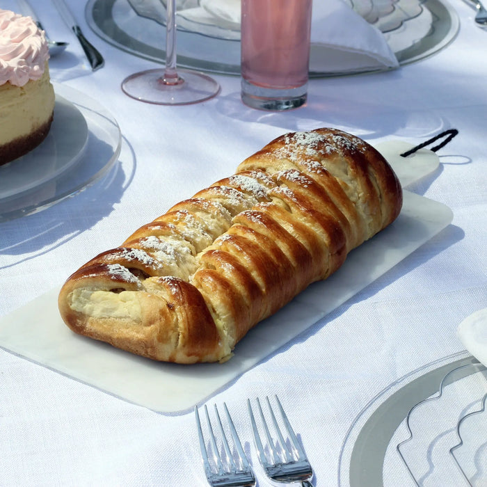 Flat marble charcuterie board displaying sliced bread and cured meats on a white tablecloth with place settings and glassware nearby.