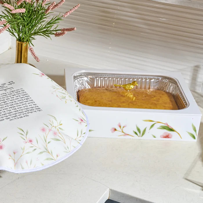 light countertop, with  a rectangular foil pan in a white acrylic  floralpan holder  holding a golden bird with a cake inside