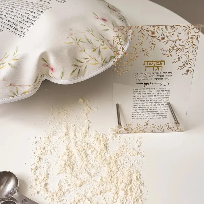 Floral Bird Challah cover in cream with delicate pink flowers and gold leaf branches, displayed with Hebrew prayer book and white powder on white surface.